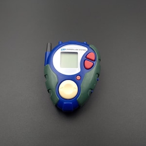 May include: A blue and green digital pet device with a screen, buttons, and a small antenna. The device has the text "Digimon Link System" on the front.