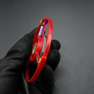 May include: Red and black plastic spinning top with a scorpion logo and the word "TRYPIO" on the side.