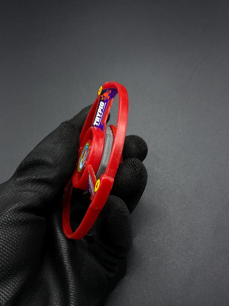 May include: Red and black plastic spinning top with a scorpion logo and the word "TRYPIO" on the side.