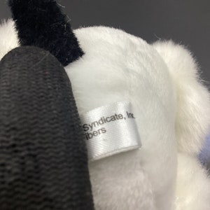 May include: White plush toy with a black tail and a white tag that reads "Syndicate, Inc. fibers".