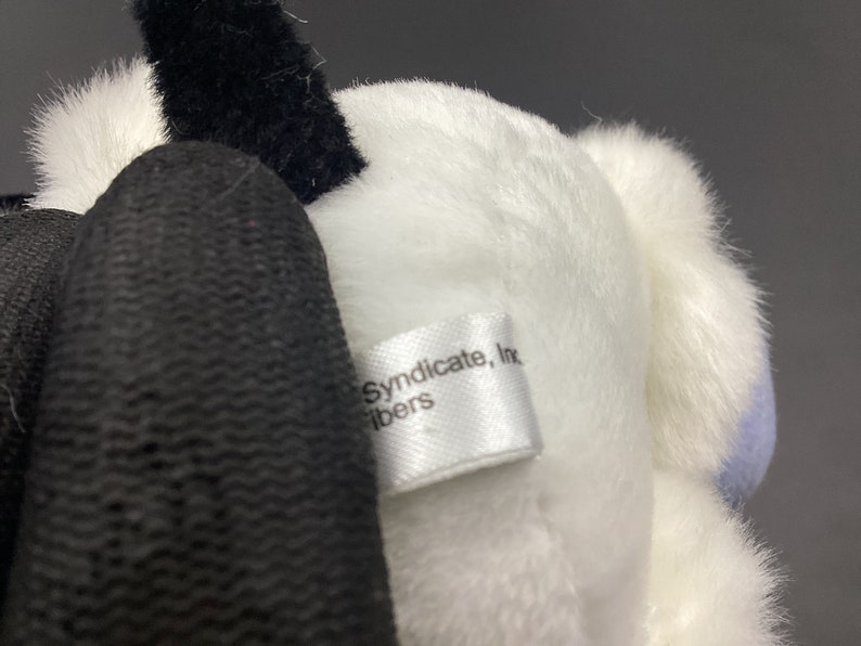 May include: White plush toy with a black tail and a white tag that reads "Syndicate, Inc. fibers".