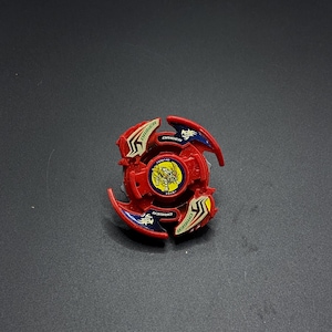 Könnte beinhalten: Rote, weiße und blaue Plastik-Beyblade mit einem Drachen-Design und dem aufgedruckten Wort "DRIGER".
