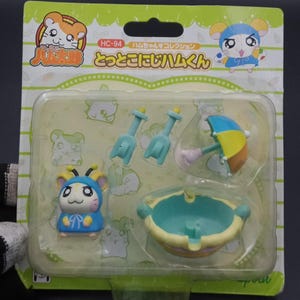 May include: A packaged toy set featuring a cartoon hamster character in a blue outfit. The set includes a small pool, two shovels, and a colorful umbrella. The packaging has Japanese text and cartoon graphics.
