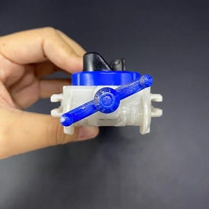 May include: A small, plastic valve with a blue handle and accents. The valve has a white body and a black top. The handle is a vibrant blue, and the overall design is simple and functional. The valve is held in a hand.