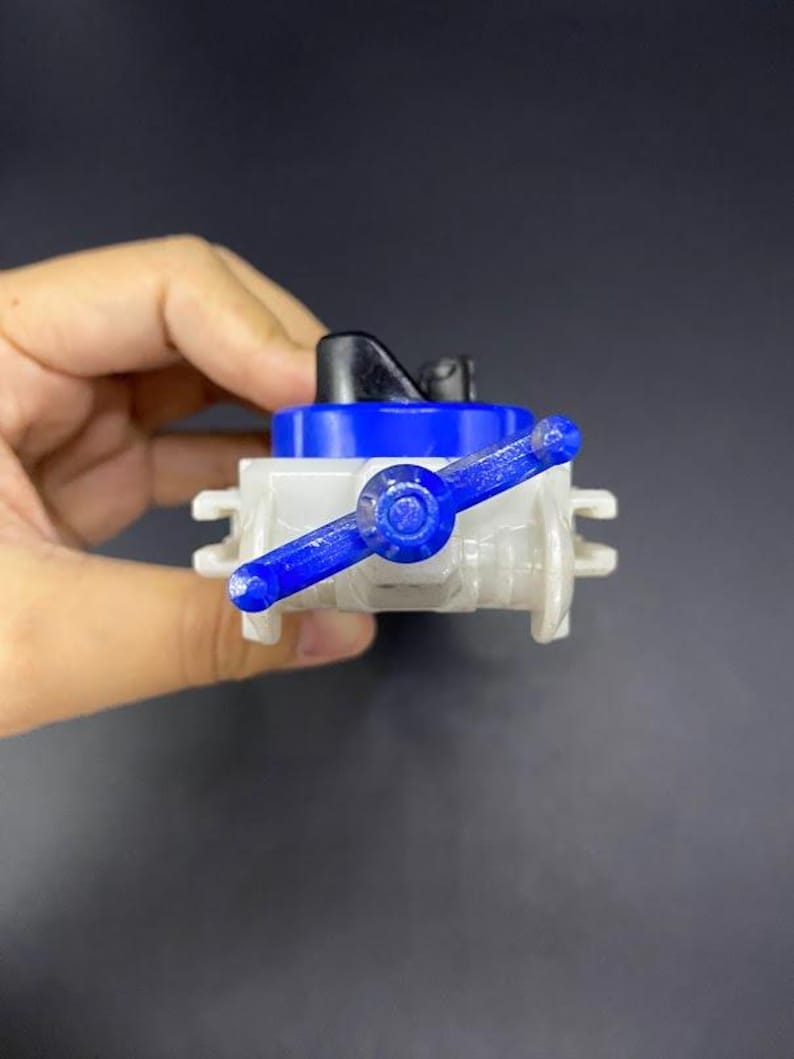 May include: A small, plastic valve with a blue handle and accents. The valve has a white body and a black top. The handle is a vibrant blue, and the overall design is simple and functional. The valve is held in a hand.