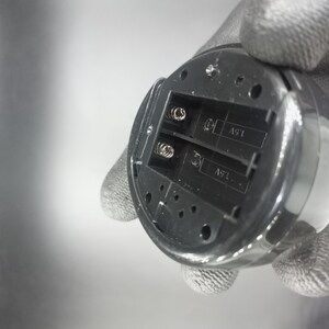 May include: Close-up of the battery compartment of a device. The compartment has two slots labeled "1.5V".