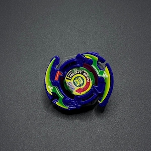 May include: A blue, green, and yellow spinning top toy. The toy has a circular design with text that reads "RIGHT SPIN" and other Japanese text. The top has a multi-layered design with a central spinning mechanism.