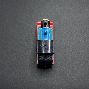 May include: A toy train with a red base, black smokestack, and blue and teal accents. The train has a small white dome and is set against a dark gray background. A classic toy.