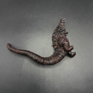 以下が含まれることがあります： 詳細なダークレッドとブラウンのゴジラのアクションフィギュア。フィギュアは、尾を丸め、口を開けたポーズをとっています。質感のある肌と詳細な特徴が、象徴的な怪物を表現しています。