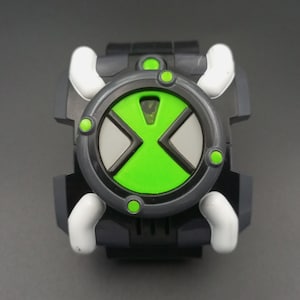 Puede incluir: Un reloj de juguete negro y gris oscuro con una esfera circular que presenta un símbolo de reloj de arena verde brillante, detalles blancos en las esquinas y pequeños puntos verdes. El dispositivo tiene un marco grueso y una correa negra.