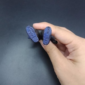 May include: Close-up of the feet of a small, dark blue action figure. The soles of the feet are visible, with the text "BANDAI 2017 CHINA" and "&copy;2017 T-T-A" imprinted on them. The figure is held against a dark background.