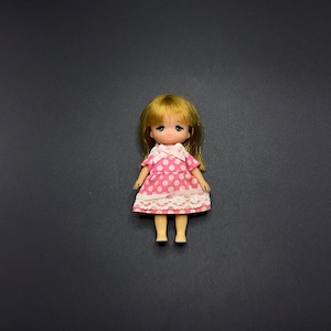 May include: A small doll with blonde hair wearing a pink dress with white polka dots and a white lace trim.