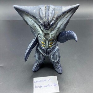 May include: A dark gray alien figurine with a triangular head and insect-like features. The figure has a detailed, textured surface with yellow accents on the chest. The figurine is standing upright. A small white paper with text is in front of the figurine.