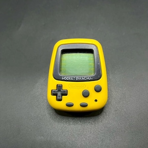 May include: A yellow Pocket Pikachu handheld electronic game. The device has a small screen, a directional pad, and several buttons. The text "POCKET PIKACHU" and "Nintendo" are visible on the device.