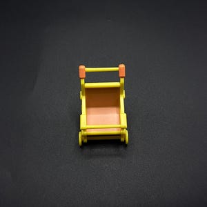May include: A miniature yellow toy pram with orange detailing. The interior is brown, and it has small wheels. The handle and side supports are orange. Designed for small dolls or toys.
