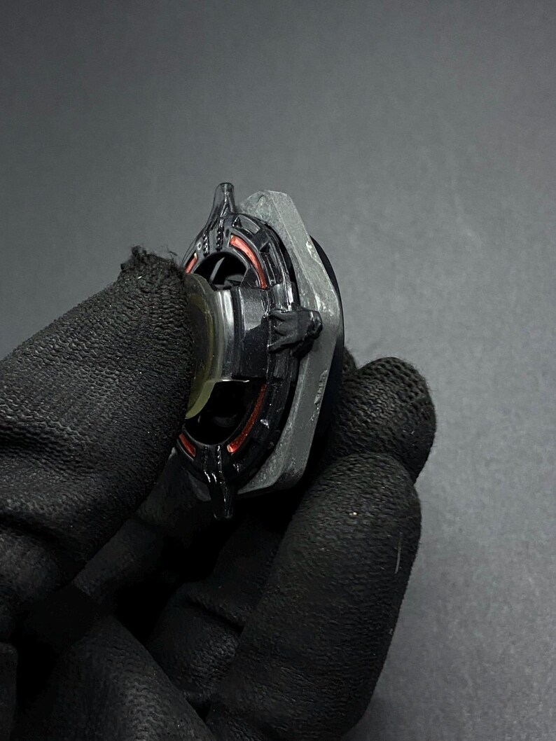 K&ouml;nnte beinhalten: Ein schwarzer und silberner Metall-Beyblade mit roten und orangen Akzenten. Der Beyblade wird in einer behandschuhten Hand gehalten.