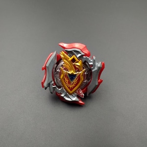 May include: A red, silver and gold spinning top toy with a shield design. The shield has a gold eagle and a blue triangle in the centre.