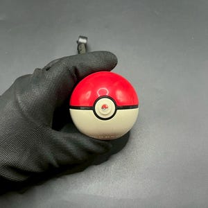 May include: A red and white Poké Ball, a spherical device used in the Pokémon franchise to capture and contain Pokémon. The top half is red, the bottom half is white, and a black band separates the two halves. A button is in the centre.