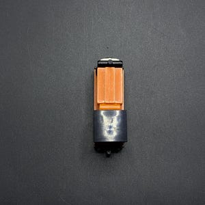 May include: A toy train car with a black and orange design. The car has a black base and a brown cargo box with a white top.