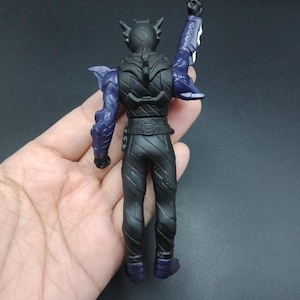 May include: A black action figure with purple accents, viewed from the back. The figure has a detailed design, including a belt, textured legs, and a raised arm. The figure's arms and shoulder blades are purple.