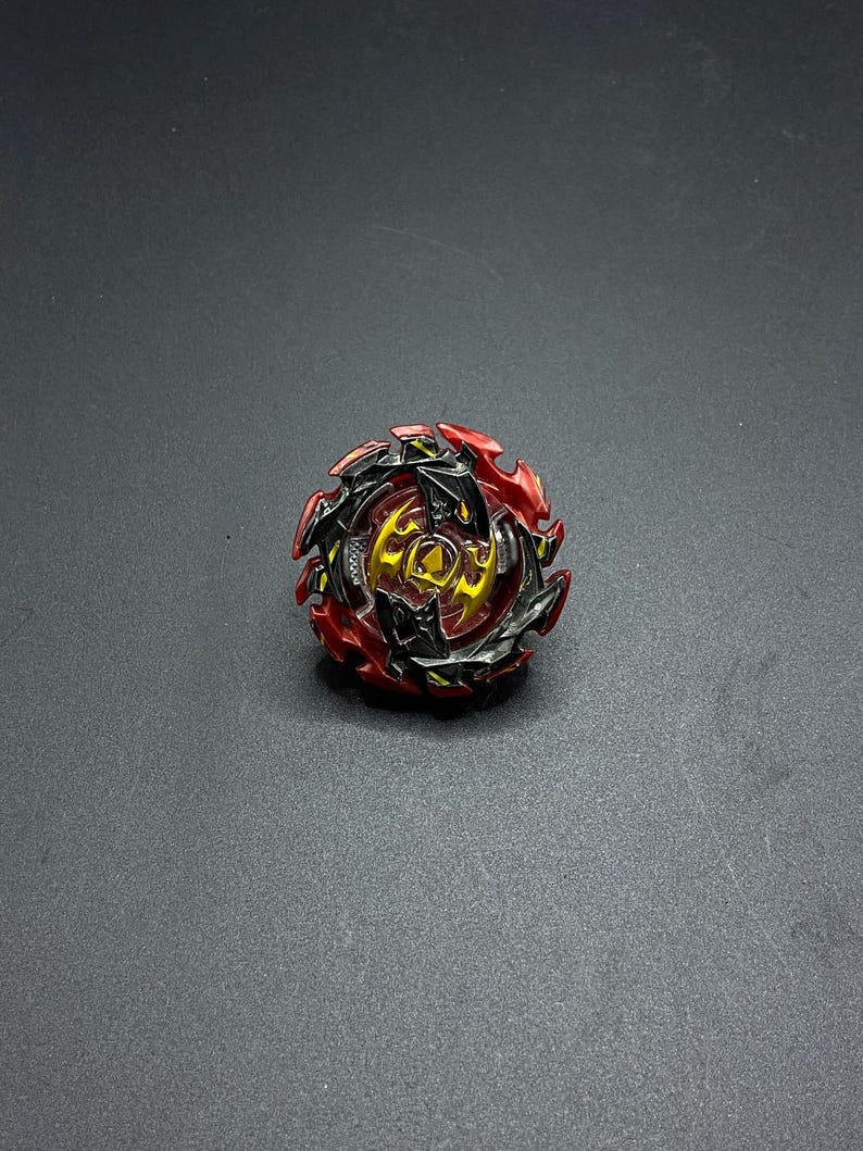 K&ouml;nnte beinhalten: Ein roter, schwarzer und goldener Kreisel mit einem scharfen, kantigen Design. Der Kreisel hat einen zentralen Kern mit einem kreisf&ouml;rmigen Design und einen Zahnkranz am Rand.