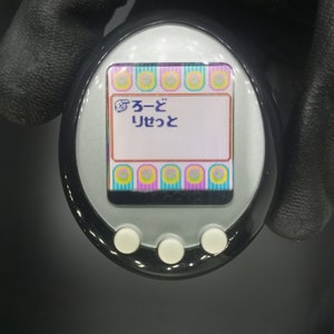 May include: A black and silver handheld electronic pet with a colorful screen displaying the Japanese text "ふーど りせっと".