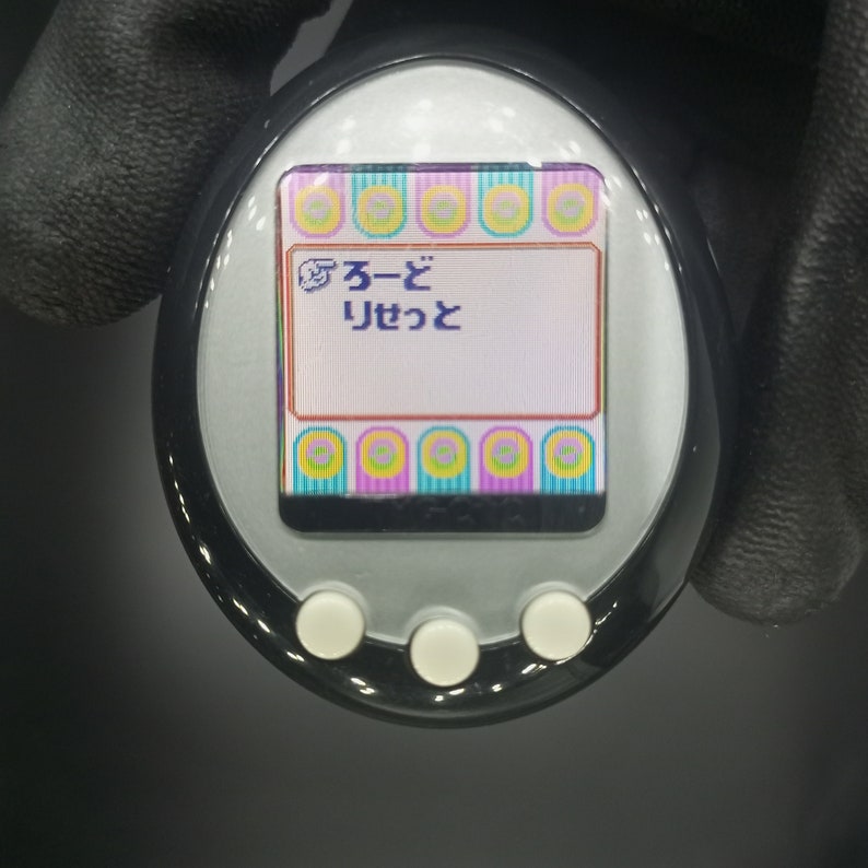 May include: A black and silver handheld electronic pet with a colorful screen displaying the Japanese text "ふーど りせっと".