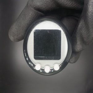 May include: Black and silver handheld electronic device with a rectangular screen and three white buttons. The device has a black border and a silver face.