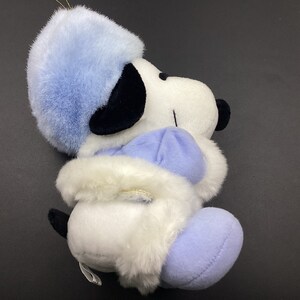 May include: A white plush toy dog wearing a blue hat and coat. The dog has black eyes and a black nose. The toy is in a sitting position.