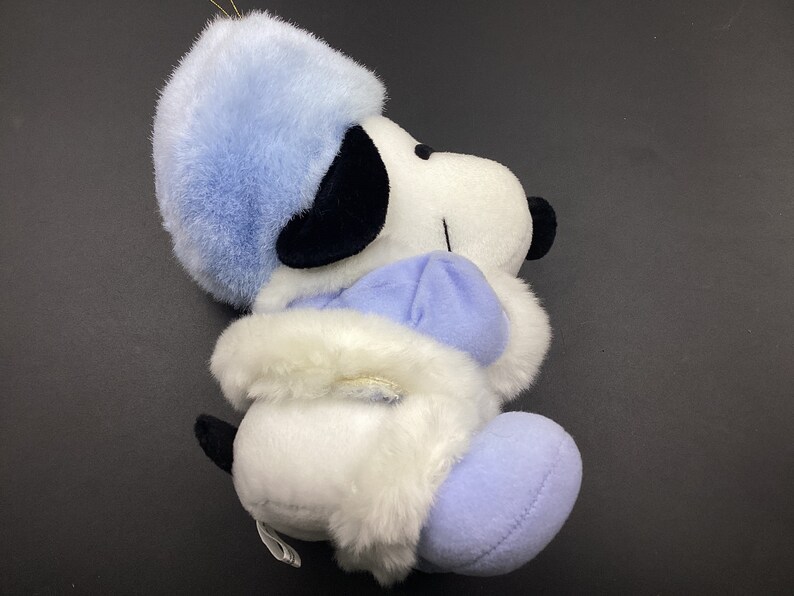 May include: A white plush toy dog wearing a blue hat and coat. The dog has black eyes and a black nose. The toy is in a sitting position.