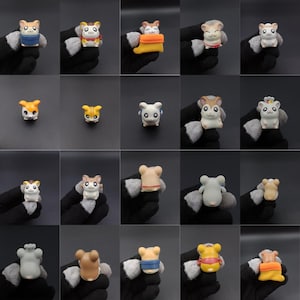 Op de afbeelding: Een verzameling kleine, kleurrijke hamsterbeeldjes. Elk beeldje is uniek ontworpen met verschillende outfits en accessoires. De hamsters staan in verschillende poses, die hun speelse en charmante uitstraling laten zien. De achtergrond is effen donker van kleur.