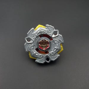 Peut inclure: Un toupie argentée et jaune avec un centre rouge et doré. Le jouet a un design circulaire avec des détails complexes et une surface texturée. Le dessus est conçu pour tourner et se battre.