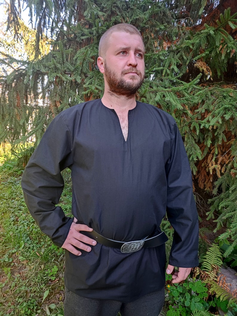 May include: A black long-sleeved shirt with a V-neck and a black leather belt with a silver buckle. The shirt is being worn by a person standing in front of a green background.
