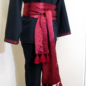May include: A black shirt with a red satin sash tied around the waist. The sash has tassels on the ends.