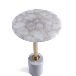 May include: A round white agate table with a gold metal base. The table top is made of natural agate and has a unique pattern. The base is a cylinder with a gold metal top.
