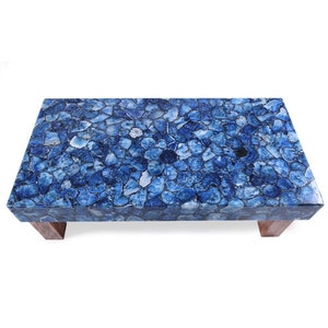 May include: A blue agate coffee table with a rectangular top and wooden legs. The table top is made of many small pieces of blue agate, creating a unique and beautiful pattern.