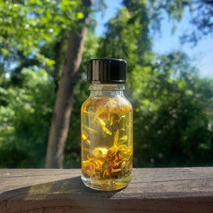 May include: A small glass bottle with a black lid filled with a yellow liquid and dried flowers. The bottle is sitting on a wooden surface.