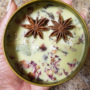 May include: A green candle with dried flowers and star anise. The candle is in a gold container.