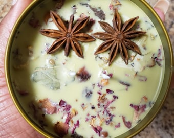 May include: A green candle with dried flowers and star anise. The candle is in a gold container.