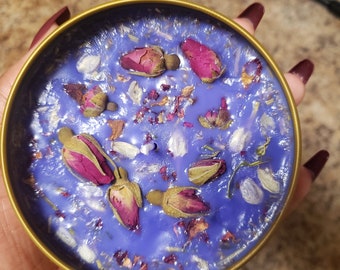 May include: A purple candle with dried rose buds and petals embedded in the wax. The candle is in a gold tin container.