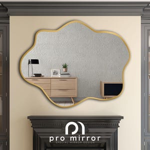 May include: A gold-framed, irregular-shaped mirror with a white, textured surface. The mirror is hanging on a wall with a dark gray cabinet on either side. The mirror reflects a wooden dresser with drawers and a television.