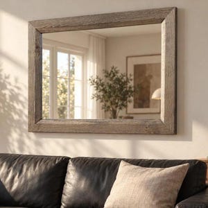 Peut inclure: Un miroir mural rectangulaire dot&eacute; d'un cadre &eacute;pais en bois gris patin&eacute; avec une texture de grain visible. La vitre du miroir refl&egrave;te un espace int&eacute;rieur lumineux avec une fen&ecirc;tre, une plante en pot et un cadre au mur.