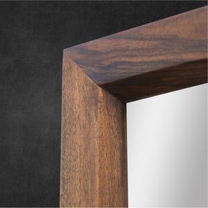 Peut inclure: Un miroir rectangulaire dot&eacute; d'un cadre &eacute;pais en bois brun fonc&eacute; avec un motif de grain naturel visible. Le cadre pr&eacute;sente des coins en onglet nets et pr&eacute;cis ainsi qu'une finition lisse, entourant une surface en verre r&eacute;fl&eacute;chissante.
