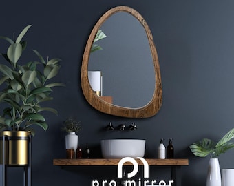 May include: A wooden framed, oval-shaped mirror with a natural wood finish. The mirror is hanging on a dark blue wall above a white porcelain sink and a wooden shelf.