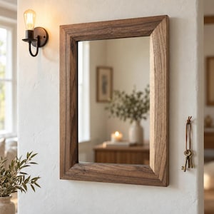 Peut inclure: Un miroir mural rectangulaire dot&eacute; d'un cadre en bois de ton moyen avec un grain visible. Le miroir est fix&eacute; sur un mur blanc &agrave; c&ocirc;t&eacute; d'une applique murale noire et d'un trousseau de cl&eacute;s en m&eacute;tal suspendu &agrave; un cordon en cuir.
