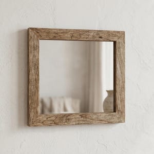 May include: Square wooden framed mirror. The frame has a natural, weathered appearance with visible wood grain and knots. The mirror reflects a soft, neutral-toned interior space. The overall aesthetic is rustic and minimalist.