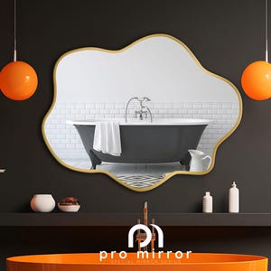 May include: A gold-framed, irregular-shaped mirror reflects a black bathtub with white tile walls. Two orange globe pendant lights hang above the mirror. The mirror is labeled "pro mirror special mirror design".