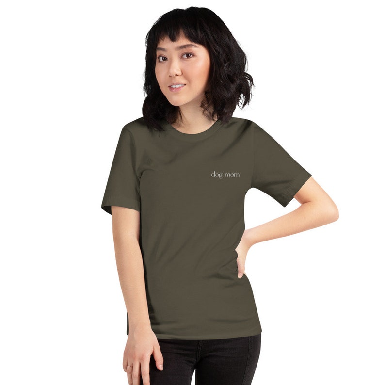 May include: A woman wearing a dark green short-sleeved t-shirt with the text "dog mom" in white lettering.