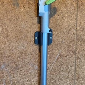 Pode incluir: Uma ferramenta de jardinagem prateada e verde com um suporte de parede preto. A ferramenta tem uma alça com um gatilho verde e o texto "EDGE" é visível na parte inferior da ferramenta.