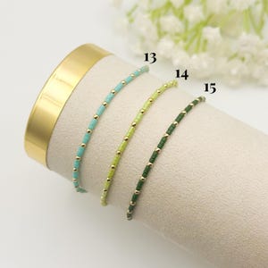 May include: Three beaded bracelets in turquoise, lime green, and dark green, each with gold-colored beads. The bracelets are displayed on a beige surface, with the numbers 13, 14, and 15 visible. The bracelets are delicate and minimalist.